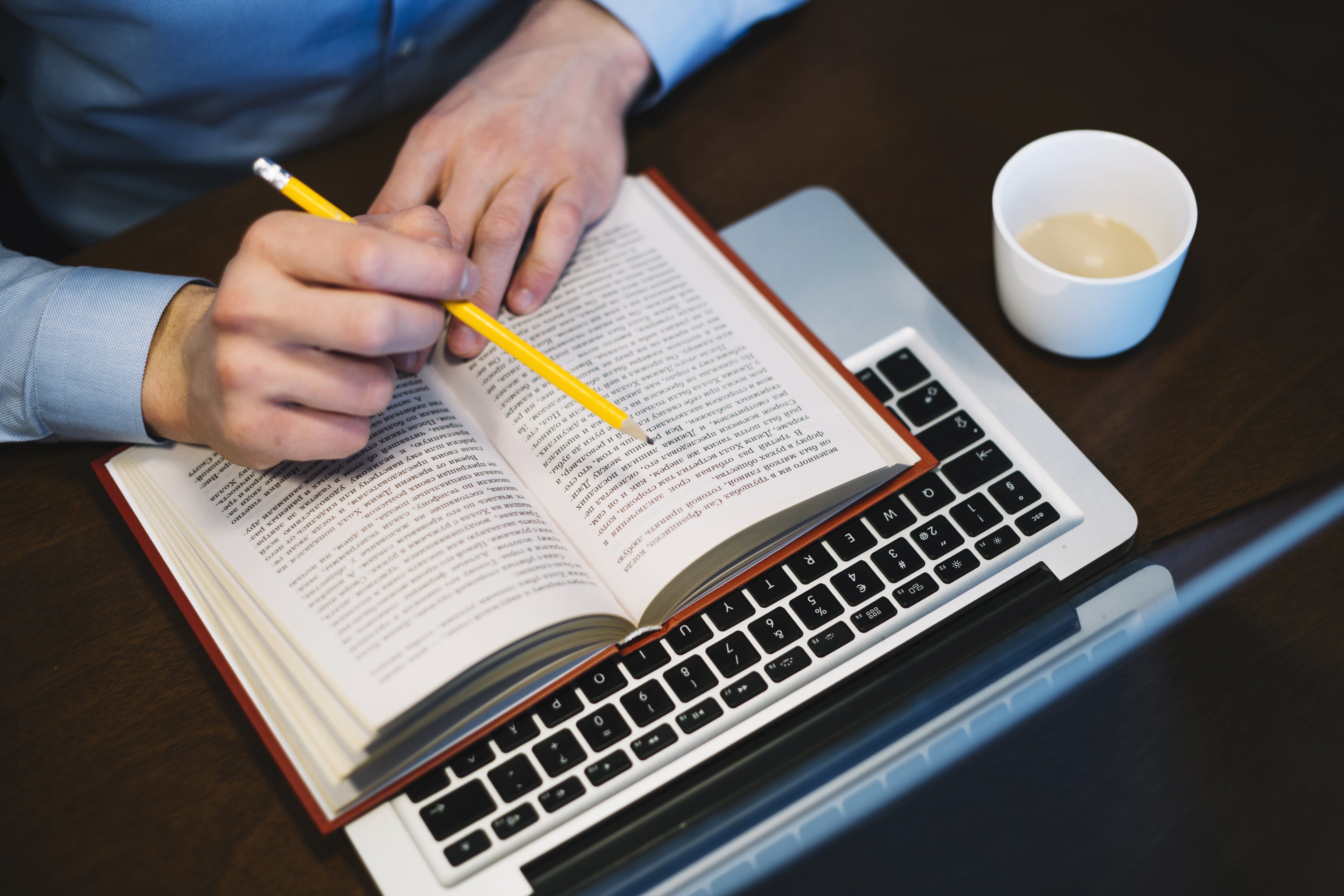 A focused man writing on a book with a pencil while enjoying a cup of coffee